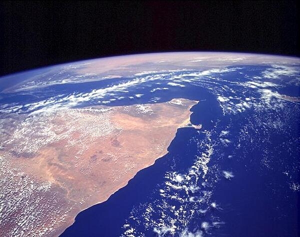 The orange and tan colors of this high-oblique photograph of the Horn of Africa indicate an arid-to-semiarid landscape in the northern half of the east African country of Somalia. Except for the darker areas where thicker vegetation can be found (usually in elevated areas), most of the vegetation in this part of Somalia is shrub brush and grasslands. The southern extent of the Saudi Arabian Peninsula is visible north across the Gulf of Aden. Image courtesy of NASA.