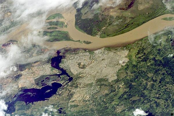 Ciudad Guayana lies on the south bank of the Orinoco River, the second largest in South America, at its confluence with the Caron&#xed; River (lower left). Islands have developed in the Orinoco in a wide spot opposite the city (upper left). Guayana is one of the newest cities in Venezuela, constructed in 1961 as a new economic center for the interior of Venezuela, especially for major industries such as iron, steel, and aluminum. The city stretches 40 km (24 mi) along the south bank of the Orinoco and is one of Venezuela&apos;s largest. A low barrage (lower left) dams the Caron&#xed; as a water supply for the city. The Orinoco River is muddy brown, carrying sediment produced by erosion of the Andes Mountains far to the southwest. By contrast, the Caron&#xed; is clear blue, as it drains the ancient landscapes of the Guyana Highlands, where erosion is much slower. A mixing zone can be seen in the middle of this image. The clear Caron&#xed; water produces a less muddy zone for tens of kilometers downstream of the confluence (this part of the Orinoco flows almost due east, left to right). Image courtesy of NASA.