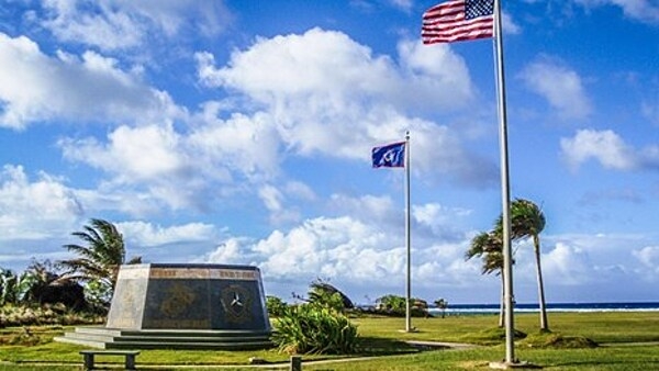 A hexagonal monument, dedicated in 1994 on the 50th anniversary of the liberation of Guam, stands in the War in the Pacific National Historical Park, under the flags of the United States and Guam. The monument's inscription reads: "Honors to heroic and gallant effort of the US Armed Forces." Photo courtesy of the US National Park Service.