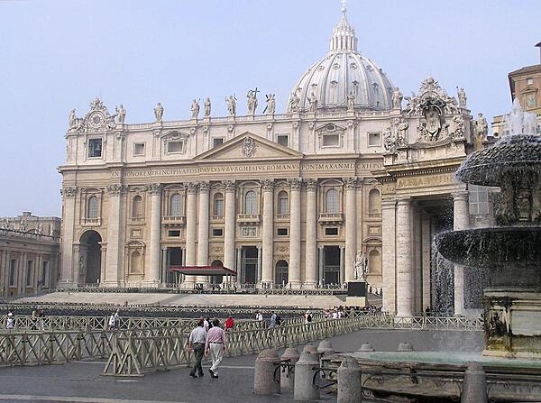 The façade of St. Peter's Basilica as viewed from one of the two matching Bernini fountains that grace St. Peter's Square (Piazza) in front of the church. The upper story displays statues of Christ, his apostles, and St. John the Baptist. Constructed over a period of 80 years and consecrated in 1626, the basilica is the largest Christian church in the world,  capable of holding some 60,000 people.