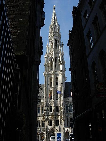 The imposing main tower of the Hotel de Ville/Stadhuis (City Hall) in Brussels, Belgium. Built in the Gothic style, parts of the structure date back to the early 15th century. Its spire is topped by a gilt metal statue of the Archangel Michael, patron saint of Brussels. The façade is decorated with statues of nobles, saints, and allegorical figures.