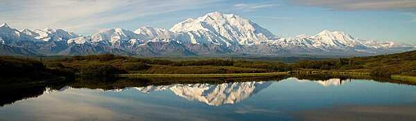 Alaska is home to North America’s highest peak, Denali, seen in the background in this picture.  Denali, at the heart of the six-million-acre Denali National Park and Preserve, stands 6,190 m (20,310 ft) above sea level and is the third-highest of the Seven Summits (the tallest peaks on all seven continents). Denali has five large glaciers flowing off its slopes. The mountain’s name comes from Koyukon, a Native Alaskan language, and means “the high one” or “the tall one.”