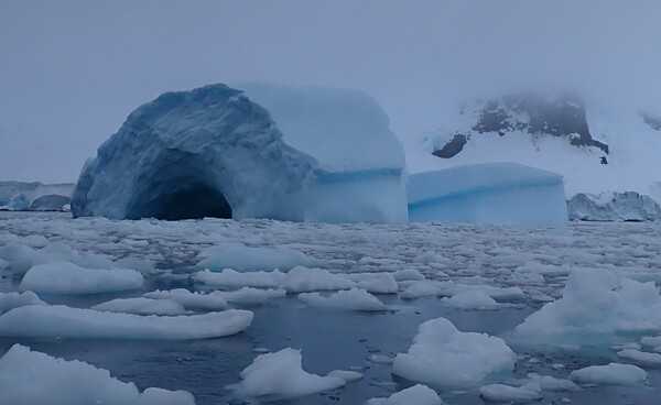 A view of the  cave-shaped iceberg in Mikkelsen Harbour of Trinity Island, in the Palmer Archipelago to the west of the Antarctic Peninsula. The loose ice in the foreground is known as "brash ice," or simply "brash."